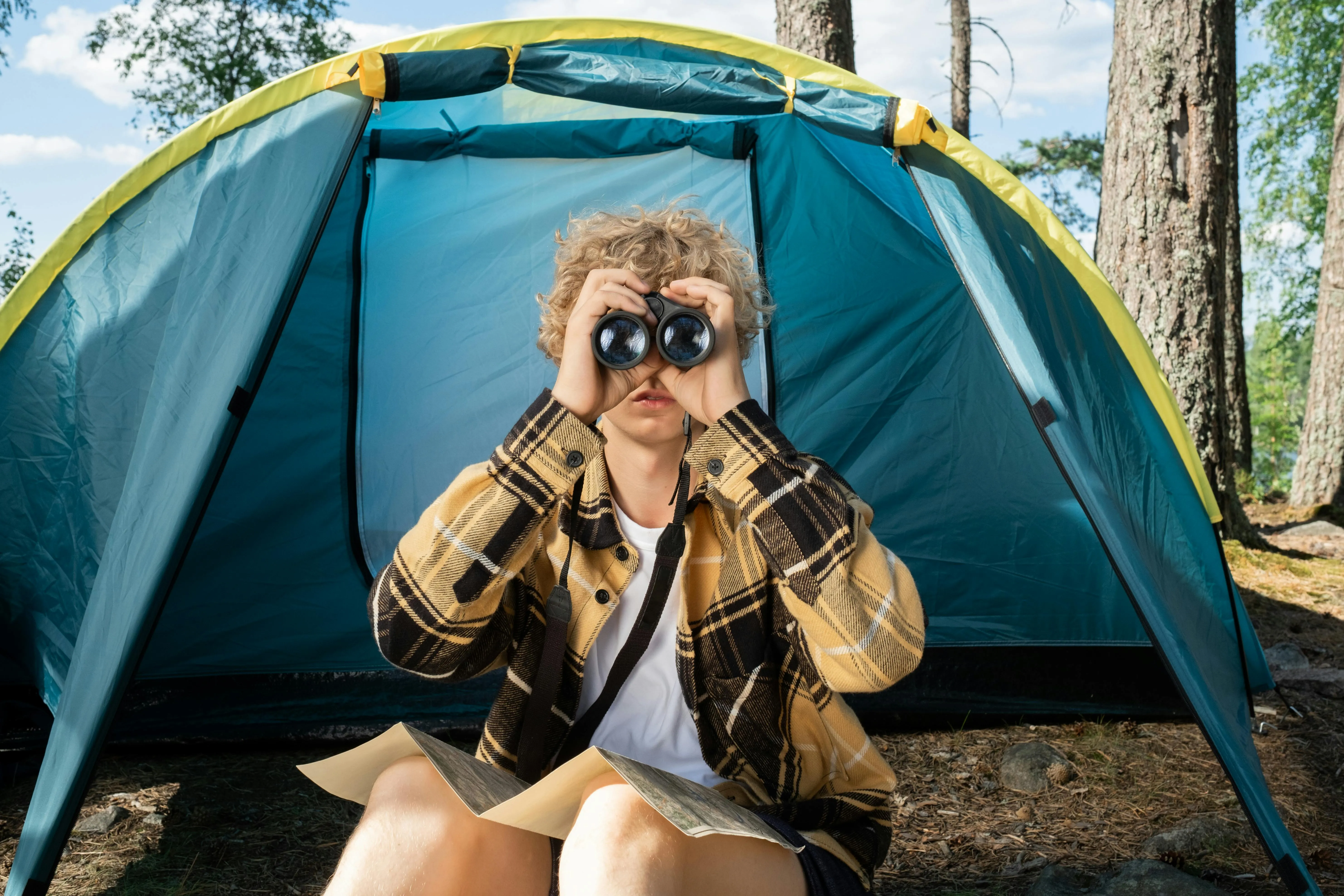 Teenager sitting outside a tent using binoculars